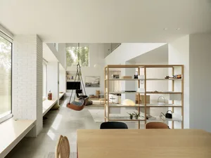 Modern minimalist living room with concrete and plaster walls and floors, featuring a hanging chair, floating shelves, and na