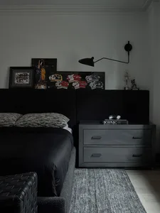A minimalist black bedroom with a upholstered bed, black nightstand, and framed posters.
