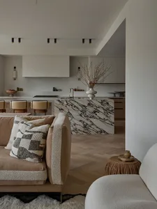 A minimalist residential kitchen features a white marble island with black veins, wooden flooring, and metal kitchen hardware