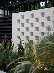 A concrete garden screen with a grid of rectangular cutouts, surrounded by greenery.