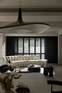 Modern living room with a neutral-colored leather sofa, black windows with blinds, and minimalist furniture.