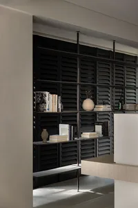A minimalist bookshelf with black shutters and metal shelves, featuring books and decorative items.