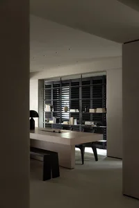 Minimalist modern workspace featuring a wooden table with a bench and black chairs, illuminated by overhead lighting, with a 
