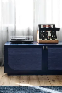 A wooden cabinet with a vinyl record player on top and a collection of vinyl records on a stand.