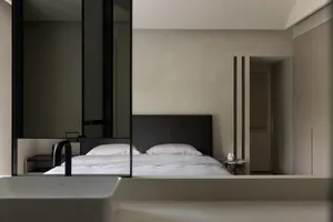 A minimalist bedroom with a white bed, black headboard, and textured walls.
