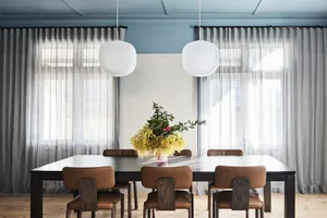 Modern dining room with glass curtains, featuring a rectangular wooden table and brown leather chairs.