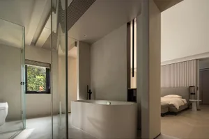 Modern minimalist bathroom featuring a concrete bathtub with a view of lush greenery outside a window.