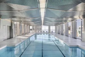 Modern interior of an indoor swimming pool with a glass ceiling and concrete floor, surrounded by tiled walls.