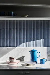 A modern kitchen featuring ceramic plates, bowls, and mugs on a marble countertop with blue accents.