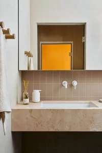 A minimalist bathroom featuring stone tiles and a modern sink with minimalist fixtures.