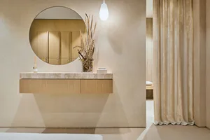 A modern bathroom featuring a marble countertop with a vase of dried plants and a round mirror above it.