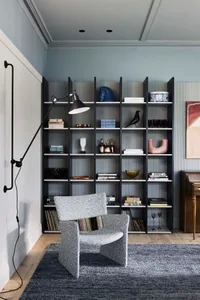 A modern minimalist living room with a grey upholstered armchair, a black and white shelving unit filled with books, decorati