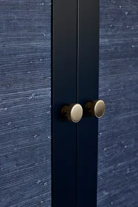 Closed cabinet with textured blue fabric on the door and two polished brass handles.
