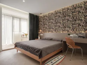 A modern bedroom featuring a bed with wooden frame and dark fabric bedding, against a wall with a floral wallpaper pattern.