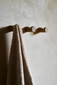 A streamlined wooden towel rack mounted on a textured white wall, with a beige towel hanging from it.