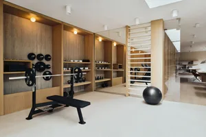 A spacious, modern gym with a minimalist design, featuring warm wood finishes, exercise equipment, and a well-organized worko