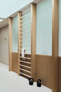 Home gym with minimalist design, featuring a wooden structure and white straps, with kettlebells on the floor.