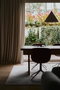 Modern dining room with wooden furniture and a floral outdoor view through a large window.