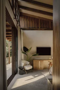 A minimalist living room features wood materials, with a white armchair, wooden cabinet, and a television mounted on the wall