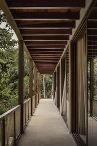 A wooden veranda patio with a roof and open sides, surrounded by tropical vegetation.