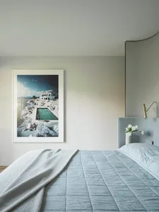A minimalist bedroom with a light blue upholstered bed and a framed photograph of a coastal landscape.