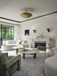 Minimalist living room featuring marble tables, a plush sofa, and a cozy fireplace, with a view of the outdoors through large
