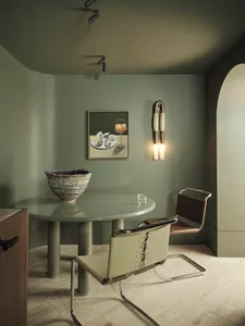A modern dining room featuring a concrete table with two chairs, a decorative vase, and a framed picture on the wall.