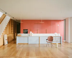 Modern kitchen with white marble countertops, brown wooden cabinets, and a plastic chair.