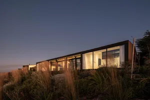 A modern house with large windows and wooden elements, illuminated at dusk.