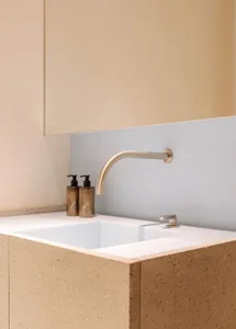 A minimalist bathroom with a white concrete sink, a brushed stainless steel faucet, and black liquid soap dispensers.
