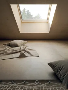 A minimalist bedroom featuring a wooden floor, pillows, and a blanket under a skylight window.