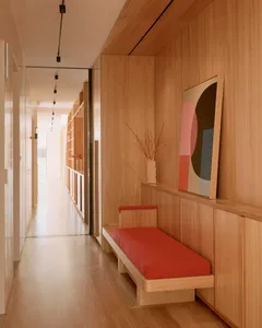 A minimalist living room with wooden walls, red cushions, and abstract painting.