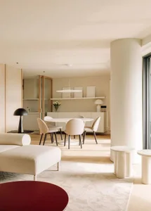 Modern, minimalist living room with neutral tones, featuring a sleek white sofa, round tables, and a dining area with a white