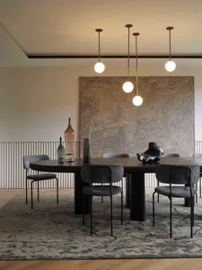 Modern dining room with metallic and glass furniture, pendant lights, and abstract wall art.
