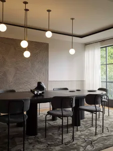 Modern dining room featuring a large round table with dark wood and metal chairs, white pendant lights, and a black and white