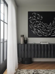 A modern interior design featuring a black console table with a textured surface and three decorative items on top, including