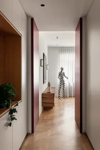 A modern interior corridor with white walls and wooden furniture, featuring a checkerboard-patterned mannequin and a plant.