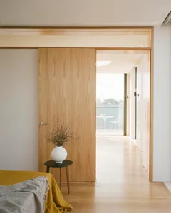 A modern minimalist bedroom with wooden finishes and a vase with dried branches on a small black side table.