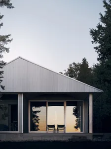 Modern minimalist exterior featuring a metal siding house with large windows and a small patio.