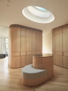 Minimalist wooden wardrobe room featuring a round glass-topped table and a curved skylight on the ceiling.
