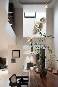 Modern living room with neutral-toned walls and floor, featuring a sleek, geometric chandelier and a mix of textures and mate