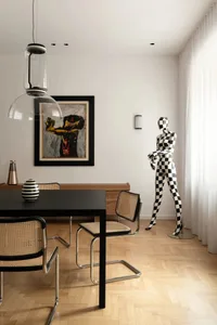 A minimalist dining room featuring a black table with woven cane chairs, herringbone wooden flooring, and a black and white c