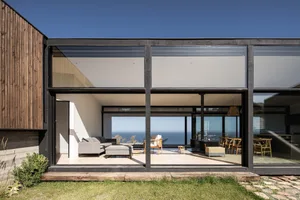 A modern residential house with large glass walls and a view of the ocean.