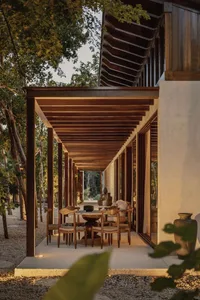 A wooden patio structure with furniture underneath, surrounded by trees and gravel.