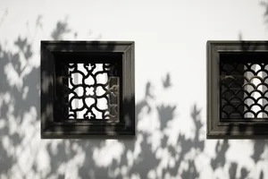 White wall with geometric patterned windows and metal frames casting shadows.
