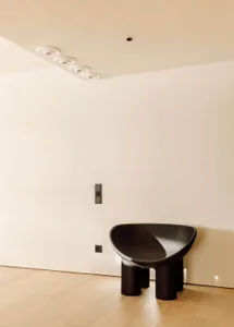 A minimalist black plastic chair in a living room with white walls and wooden floor.