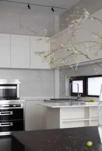 A modern minimalist residential kitchen with white cabinetry, marble countertops, and stainless steel appliances.