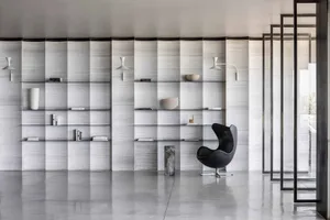 A minimalist bedroom featuring concrete walls, glass shelving, and a black armchair.