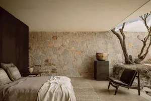 A minimalist bedroom featuring a stone wall, concrete floor, and natural surroundings with trees.
