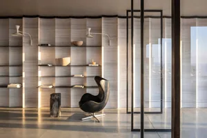 A minimalist modern interior with concrete walls, glass partition, and a leather chair.